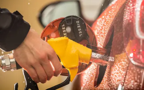 Mano che inserisce la pompa del **diesel nella benzina**. Gocce d'acqua sulla carrozzeria arancione.