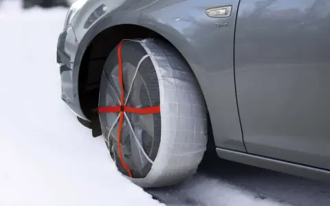 Calze da neve omologate in Italia montate su un'auto grigia su strada innevata.