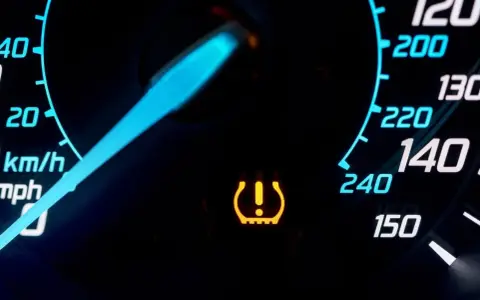 Cruscotto auto con spia pressione gomme accesa. L'indicatore giallo segnala un problema, forse un pneumatico sgonfio.