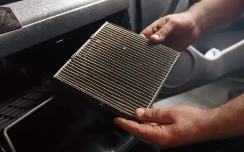 Mani che estraggono un filtro abitacolo sporco, suggerendo la necessità di cambiarlo.