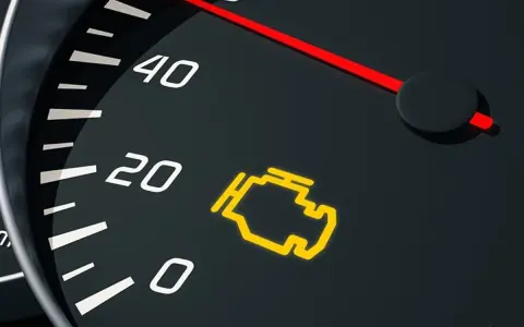 Cruscotto auto con spia olio arancione accesa. L'indicatore del motore è illuminato, segnalando un problema.