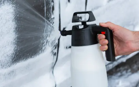 Mano che spruzza schiuma per lavare auto a casa con un erogatore.