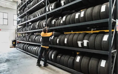 Un uomo in magazzino controlla il deposito pneumatici. Scaffali pieni di gomme, pronte per essere montate.