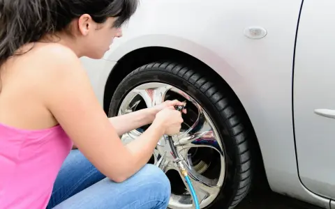 Donna controlla la pressione gomme auto estate, gonfiando uno pneumatico con un compressore.
