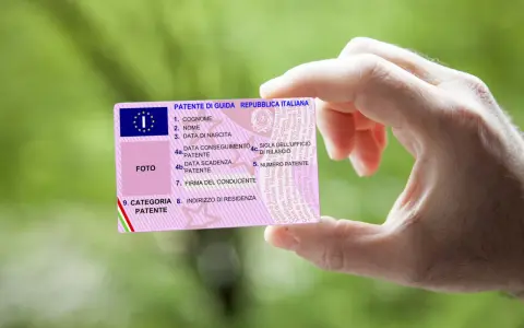 Mano che tiene una patente italiana, con dettagli su nome, data di nascita e scadenza. Nuove regole patente in arrivo?