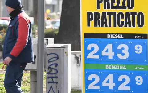 Prezzo praticato per la benzina: 2,429 €/litro. Un uomo in divisa osserva il cartello.
