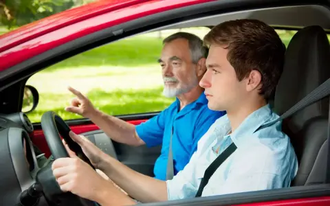 Un giovane neopatentato al volante, con un accompagnatore anziano che indica la strada.