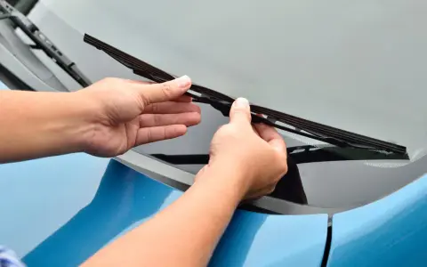Mani che sostituiscono un tergicristallo sul parabrezza di un'auto blu. Guida rapida su come cambiare tergicristalli.