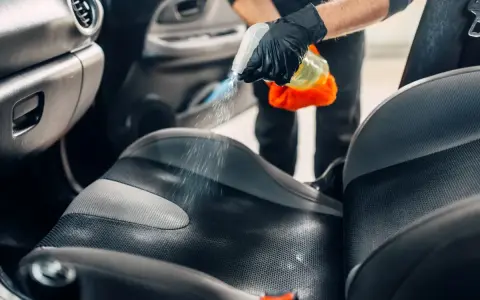 Mani guantate spruzzano detergente sul sedile dell'auto per pulire vomito.