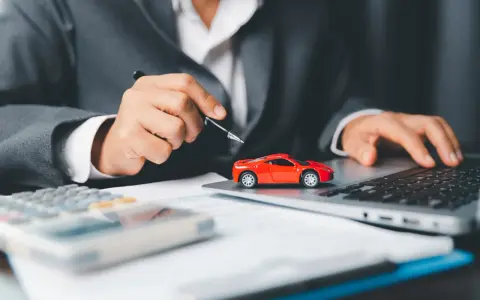 Persona in giacca grigia analizza costi auto con calcolatrice e laptop, accanto a un modellino rosso. Si chiede ogni quanto si paga il bollo auto.
