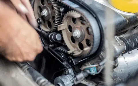 Mano che lavora sul motore, ingranaggi e cinghia di distribuzione. Scopri quanto costa cambiare la cinghia di distribuzione per la tua auto.