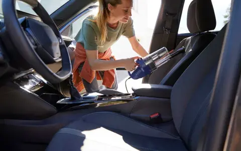 Donna usa un aspirapolvere portatile per pulire i sedili dell'auto, rimuovendo polvere e briciole per un interno impeccabile.