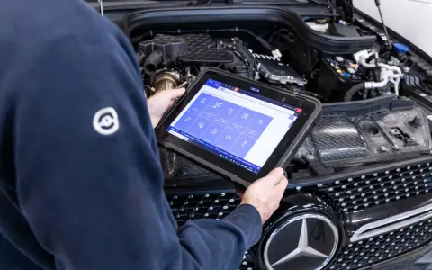 Meccanico usa tablet per diagnosi auto. Il display mostra icone per controlli e manutenzione, suggerendo quanto dura la revisione auto.