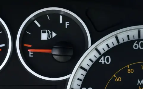Cruscotto auto con indicatore carburante quasi vuoto, la spia pompa benzina è accesa.