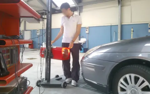 Tecnico effettua la revisione auto ibride in officina, regolando un faro con apparecchiatura specifica.
