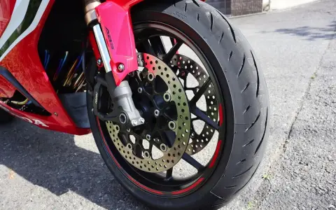 Ruota anteriore di una moto rossa, con disco freno forato e pinza ABS. Il volante che vibra a bassa velocità è un dettaglio che si percepisce.