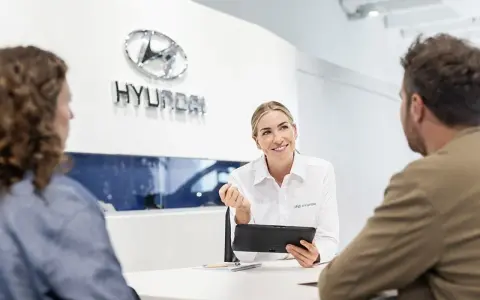 Venditrice Hyundai sorridente mostra un tablet a una coppia, discutendo il tagliando della loro auto.