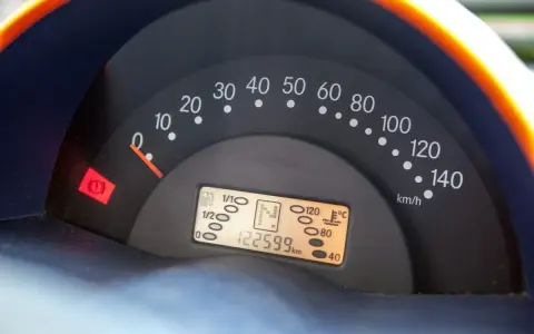 Cruscotto auto con tachimetro e spia del freno di stazionamento accesa. Chilometraggio 122599 km.