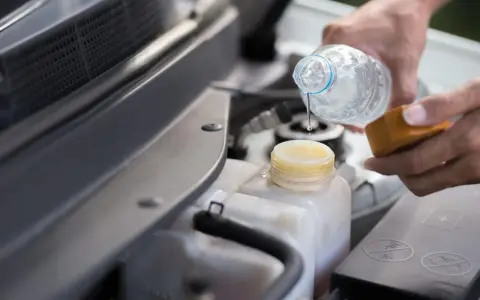 Mani versano acqua distillata nel serbatoio del radiatore dell'auto, un gesto di cura per il motore.