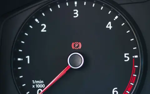 Cruscotto auto con tachimetro e spia freno a mano accesa.