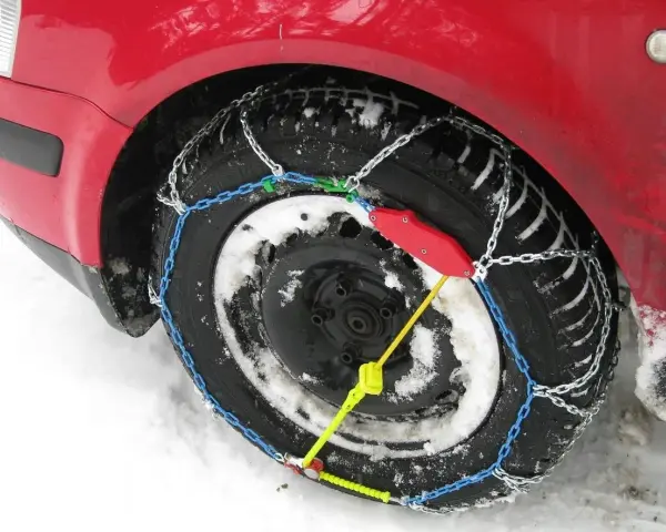 Ecco come mettere le catene da neve: una ruota di un'auto rossa coperta di neve con catene montate.