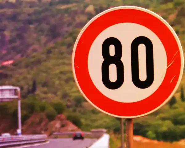 Segnale di limite massimo nei centri abitati: 80 km/h. Strada panoramica con vegetazione sullo sfondo.