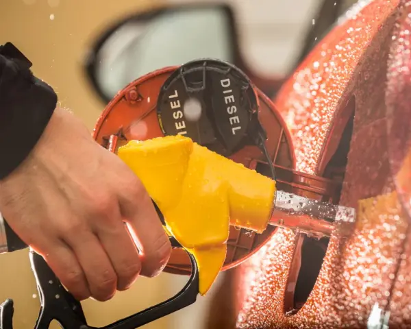 Mano che inserisce la pompa del **diesel nella benzina**. Gocce d'acqua sulla carrozzeria arancione.