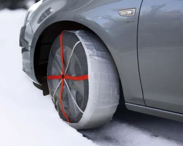 Calze da neve omologate in Italia montate su un'auto grigia su strada innevata.