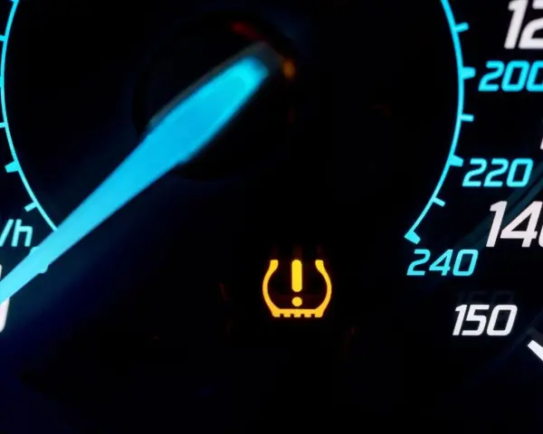 Cruscotto auto con spia pressione gomme accesa. L'indicatore giallo segnala un problema, forse un pneumatico sgonfio.