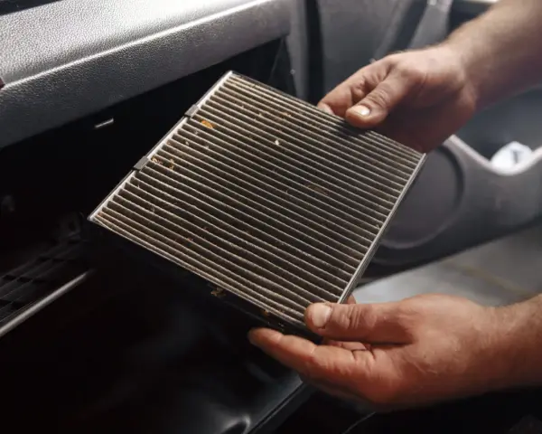 Mani che estraggono un filtro abitacolo sporco, suggerendo la necessità di cambiarlo.