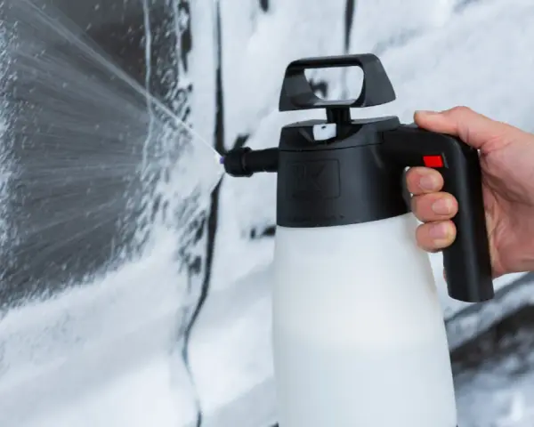 Mano che spruzza schiuma per lavare auto a casa con un erogatore.