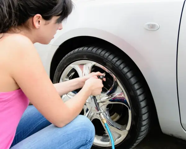 Donna controlla la pressione gomme auto estate, gonfiando uno pneumatico con un compressore.
