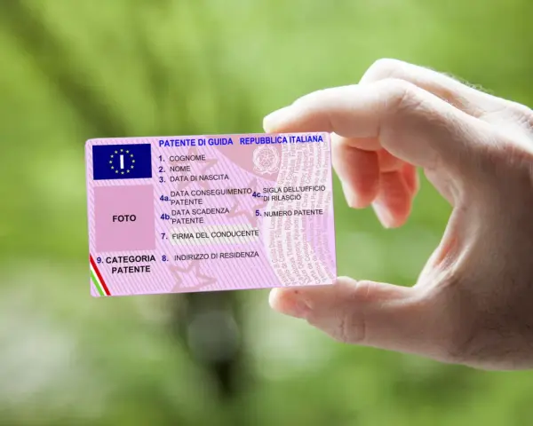 Mano che tiene una patente italiana, con dettagli su nome, data di nascita e scadenza. Nuove regole patente in arrivo?