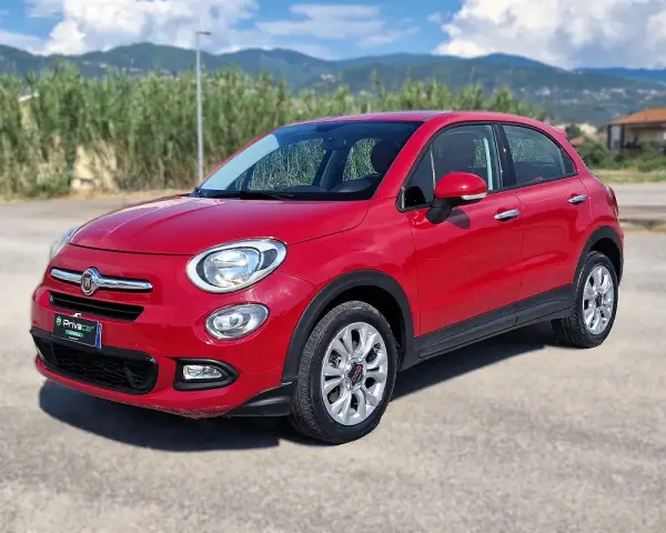 Fiat 500X rossa parcheggiata all'aperto, con montagne sullo sfondo. Controlla la pressione pneumatici per un viaggio sicuro.