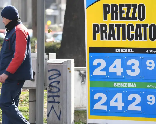 Prezzo praticato per la benzina: 2,429 €/litro. Un uomo in divisa osserva il cartello.