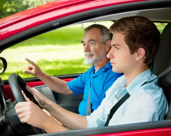 Un giovane neopatentato al volante, con un accompagnatore anziano che indica la strada.