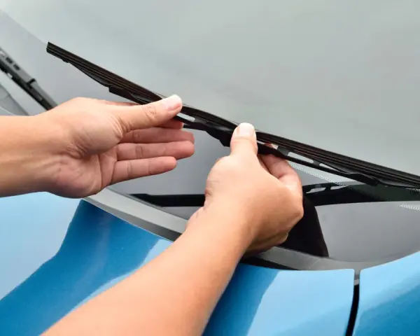 Mani che sostituiscono un tergicristallo sul parabrezza di un'auto blu. Guida rapida su come cambiare tergicristalli.