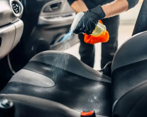 Mani guantate spruzzano detergente sul sedile dell'auto per pulire vomito.
