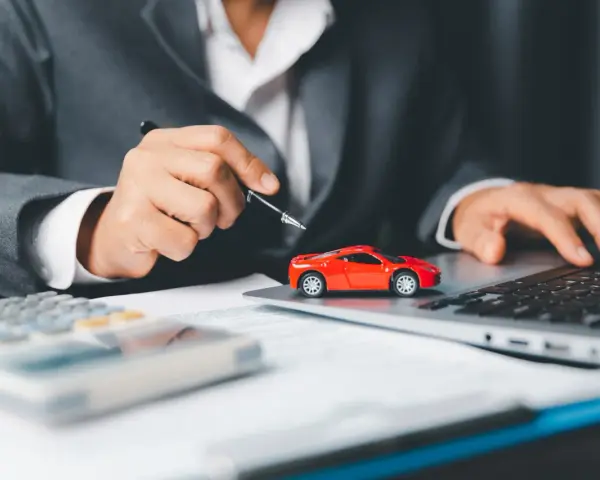 Persona in giacca grigia analizza costi auto con calcolatrice e laptop, accanto a un modellino rosso. Si chiede ogni quanto si paga il bollo auto.
