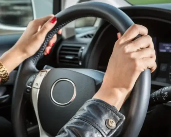 Mani con smalto rosso e bracciale d'oro tengono il volante. Il cruscotto mostra la velocità, definendo cosa vuol dire anteriore in un'auto.