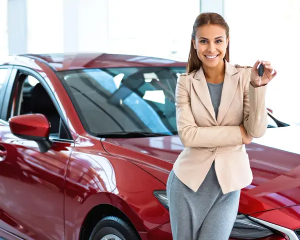 Donna sorridente con le chiavi in mano, accanto a una nuova auto rossa, pronta per il rodaggio.