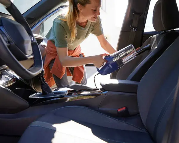 Donna usa un aspirapolvere portatile per pulire i sedili dell'auto, rimuovendo polvere e briciole per un interno impeccabile.