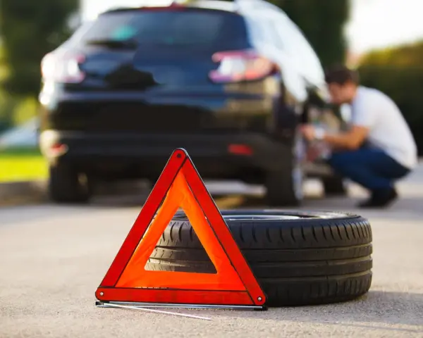 Triangolo di emergenza e ruota sgonfia accanto a un'auto nera, con un uomo che lavora alla ruota posteriore.