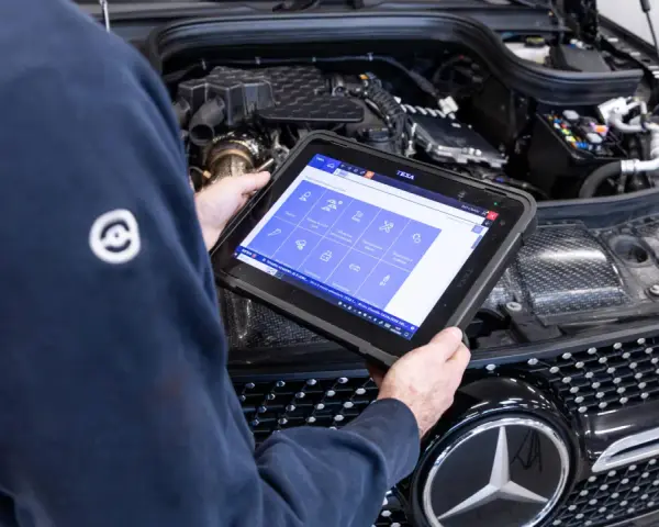 Meccanico usa tablet per diagnosi auto. Il display mostra icone per controlli e manutenzione, suggerendo quanto dura la revisione auto.