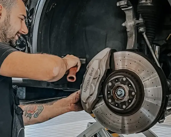 Meccanico sorridente effettua manutenzione a3 Mercedes, concentrato sul freno a disco forato e pinza con logo.