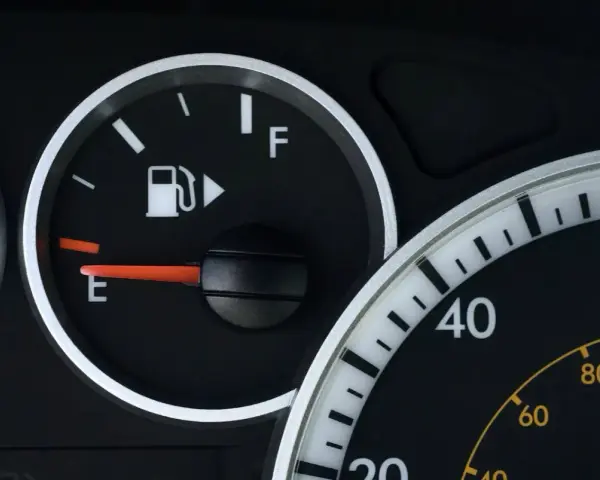 Cruscotto auto con indicatore carburante quasi vuoto, la spia pompa benzina è accesa.