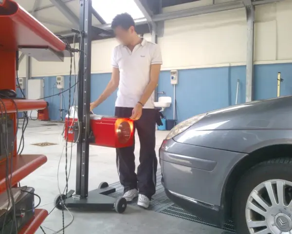 Tecnico effettua la revisione auto ibride in officina, regolando un faro con apparecchiatura specifica.