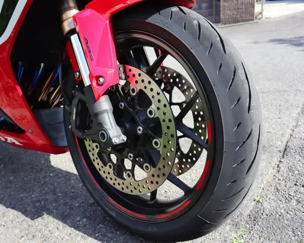 Ruota anteriore di una moto rossa, con disco freno forato e pinza ABS. Il volante che vibra a bassa velocità è un dettaglio che si percepisce.
