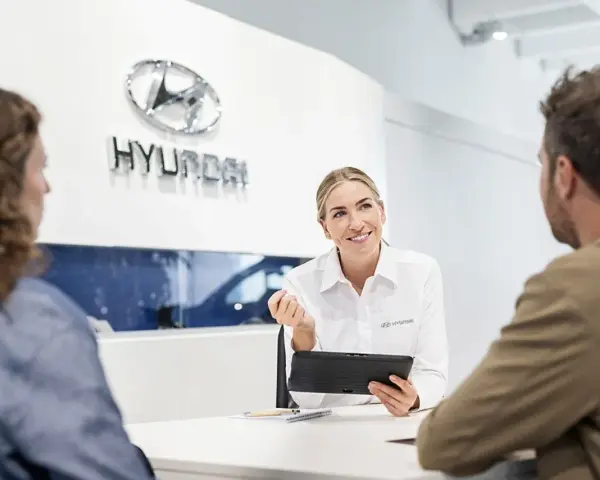 Venditrice Hyundai sorridente mostra un tablet a una coppia, discutendo il tagliando della loro auto.