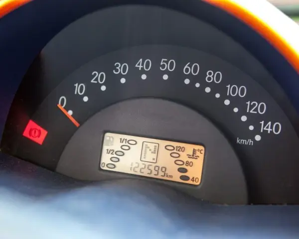 Cruscotto auto con tachimetro e spia del freno di stazionamento accesa. Chilometraggio 122599 km.